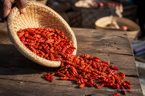 Piments pili pili séchés de Madagascar versés d'un panier tressé sur une table en bois